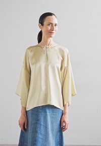 Beige μεταξωτή μπλούζα με φαρδιά μανίκια και λαιμόκοψη σε σχήμα βάρκας, συνδυασμένη με μπλε τζιν φούστα. Απλός σχεδιασμός με ελάχιστες διακοσμήσεις.