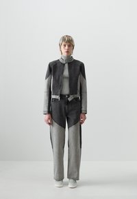 Conjunto de chaqueta y pantalones de mezclilla gris, que presenta paneles en negro y gris contrastantes, un alto cuello, cierre de cremallera y zapatillas blancas. Textura suave.