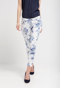 Pantalón largo de tela blanca con estampado floral azul; combinado con una blusa azul marino y tacones oscuros.