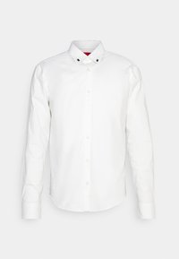 Chemise blanche à manches longues avec boutonnière, col pointu et petits accents noirs sur le col. Texture lisse et coupe ajustée.