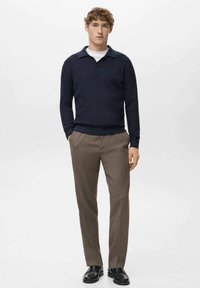 Gebreide marineblauwe trui met kraag, gecombineerd met beige broek en zwarte schoenen, met een ontspannen pasvorm en een textuurvolle stof.