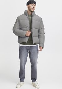 Gray, puffy jacket with a high collar, paired with a green sweatshirt, light gray denim jeans, and white sneakers. Simple design, casual fit.