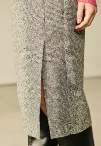 Grå tekstureret nederdel med en sidelæg, der viser et vævet mønster. En lyserød langærmet top er synlig og tilføjer kontrast til outfittet.