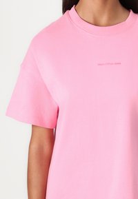 Roze katoenen t-shirt met korte mouwen en een ronde halslijn. Heeft subtiele "Marc O'Polo DENIM" branding in het midden. Zachte textuur.