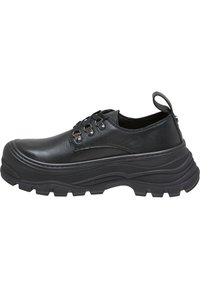 Chaussures basses noires en cuir avec des semelles en caoutchouc texturé, dotées d'un bout arrondi, d'un laçage et d'une boucle au talon.