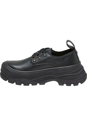 Chaussures basses noires en cuir avec des semelles en caoutchouc texturé, dotées d'un bout arrondi, d'un laçage et d'une boucle au talon.