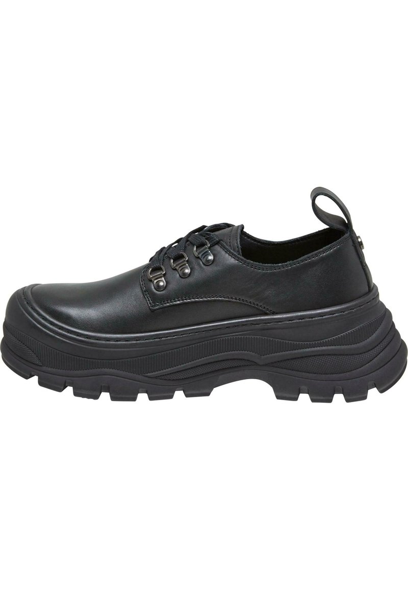 Chaussures basses noires en cuir avec des semelles en caoutchouc texturé, dotées d'un bout arrondi, d'un laçage et d'une boucle au talon.