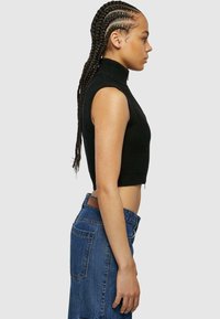 Čierny rebrovaný bezrukávový crop top s vysokým golierom, skombinovaný s vysokými modrými džínsami z denimu so zadnou vreckom a koženou nášivkou.