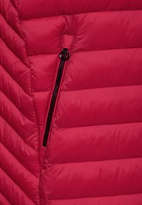 Rote isolierte Jacke mit horizontalem Steppmuster, ausgestattet mit einer seitlichen Reißverschlusstasche mit schwarzem Reißverschluss. Glattes, glänzendes Außenmaterial.
