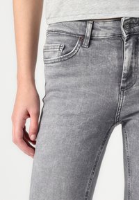 Gray denim jeans with a slim fit, featuring five pockets, a button closure, and noticeable fading for a vintage look.