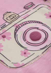 Rosa stof med et blomsterkameradesign, der har et tekstureret objektiv og glitrende accenter. Glat overflade med hævede pink blomsterdetaljer.
