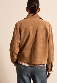 Braune Wildleder-Cropped-Jacke mit Reverskragen, sichtbaren Nahtdetails und einer glatten Oberfläche, kombiniert mit blauen Denim-Jeans.