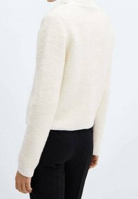 Teksturowany biały sweter z okrągłym dekoltem, ściśniętym dołem i długimi rękawami, noszony na czarnych spodniach, prezentujący luźny krój.