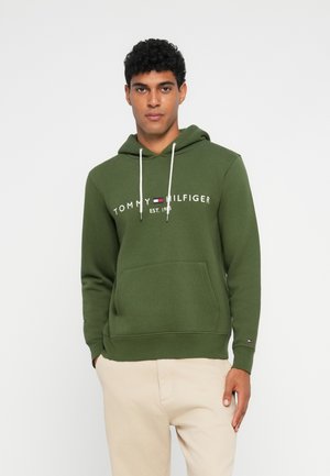 Zöld kapucnis pulóver kenguruzsebbel; fehér "Tommy Hilfiger" logóval és alapítási dátummal, zsinóros kapucnival és bordás mandzsettákkal.