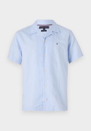 Helles blaues Kurzarmhemd aus einem Stoff mit weicher Textur. Verfügt über einen spitzen Kragen, eine Knopfleiste und ein kleines Logo auf der Brust.