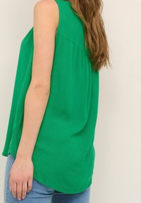 Top sin mangas verde hecho de una tela ligera, con un corte relajado, un dobladillo curvado y sutiles detalles de textura vertical.