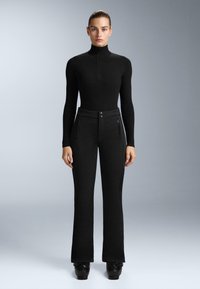 Fekete, hosszú ujjú felső negyed cipzárral, magas derékú fekete nadrággal párosítva, oldalzsebekkel és bővülő szárú kialakítással.