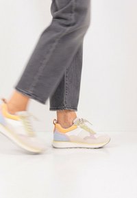 Baskets sportives présentant un design en matériaux mixtes avec des couleurs pastel, une semelle texturée, et des accents légers en rose, jaune et bleu.