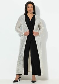 Cárdigan largo de lentejuelas en plata sobre una blusa negra y pantalones de pierna ancha. Tejido suave con una textura brillante, abertura frontal y mangas largas.