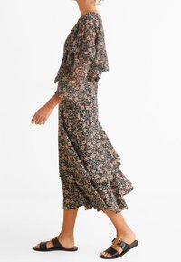 Robe fleurie avec des manches volantées, fond noir et motif de fleurs rose-orange. Complétée par des sandales plates noires avec un détail de boucle.