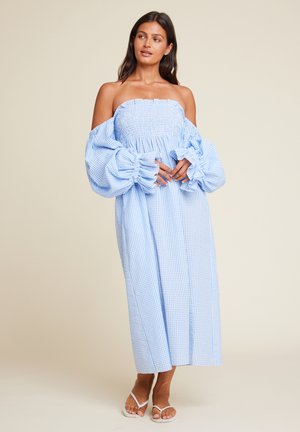 Blå og hvit gingham midi kjole med smokkete bodice og overdimensjonerte pufferm. Flytende stoff, stroppeløs design, flate sandaler på.