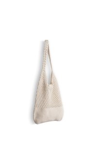 Sac de marché réutilisable beige au crochet, avec une section supérieure en maille ouverte et un fond en tricot solide, suspendu par sa sangle.