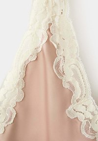 Tissu beige avec une délicate bordure en dentelle écrue présentant des motifs floraux et en résille, créant un contraste de texture doux et élégant.