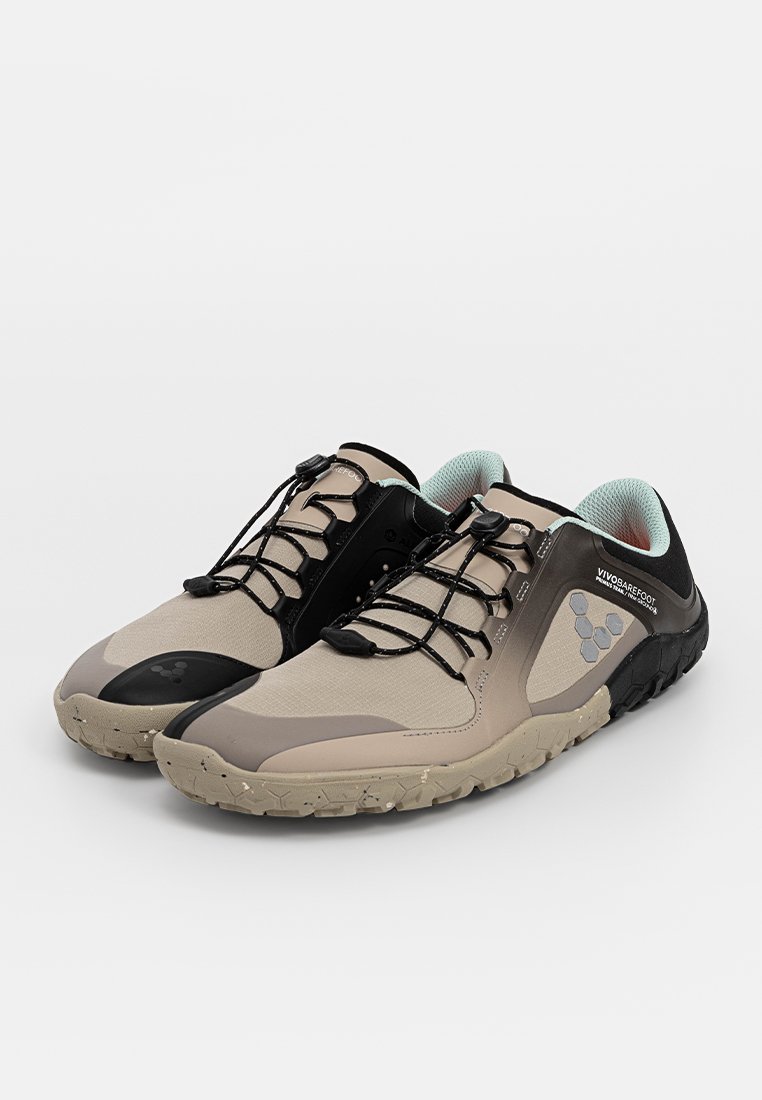 Zapatos ligeros beige y negros con suela texturizada, cordones elásticos y cuello acolchado; diseñados para ofrecer flexibilidad y comodidad.