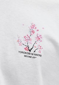 Zweig mit rosa Kirschblüten und fallenden Blütenblättern über dem Text "Yorokobi Ni Naere" und "Become Joy" auf weißem Stoffhintergrund.