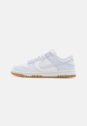 Hvid low-top Nike sneaker med lyseblå teksturerede overlays, hvide snørebånd, en hvid mellemsål og en brun gummi ydersål.
