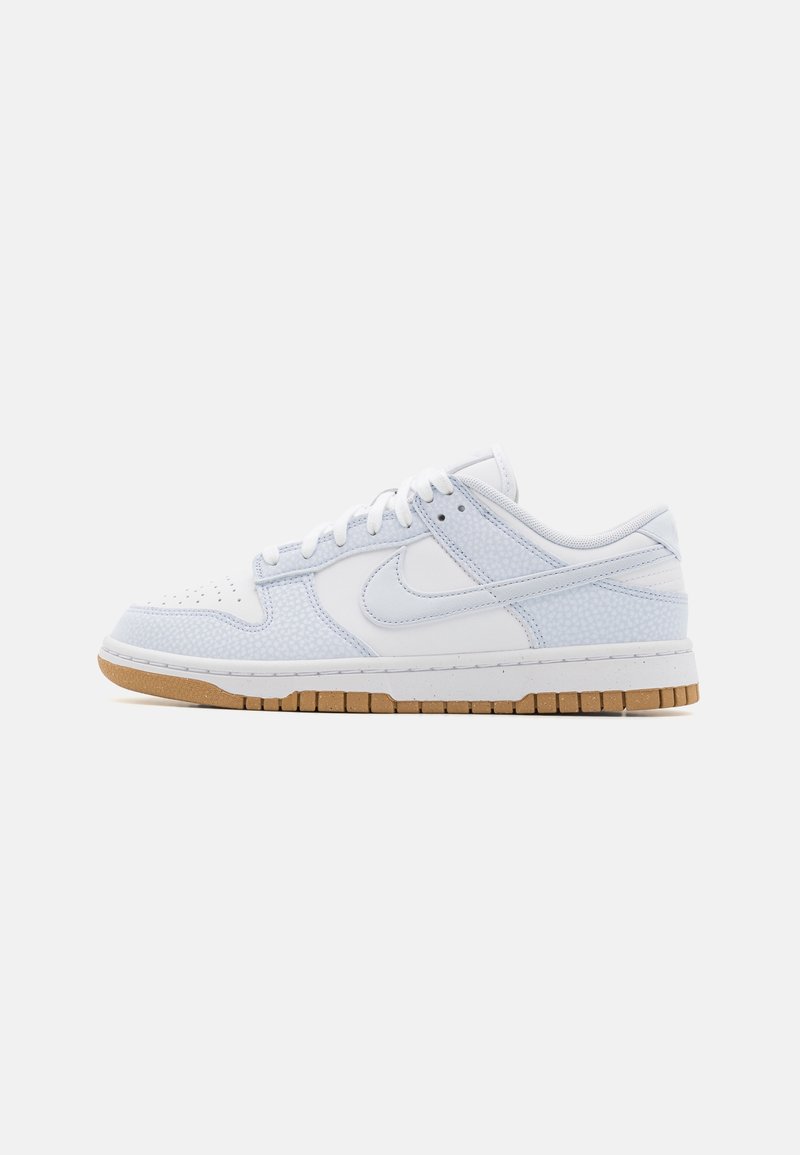 Baskets basses blanches Nike avec des superpositions texturées bleu clair, des lacets blancs, une semelle intermédiaire blanche et une semelle extérieure en caoutchouc marron.