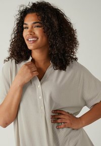 Camisa de manga corta gris claro con un ajuste holgado, que presenta un discreto patrón a cuadros y una tapeta de tres botones en el escote.