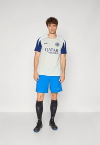 Fußballtrikot mit einem hellgrauen Trikot mit blauen Akzenten, Logo und Schriftzug; blaue Shorts; schwarze Socken; und schwarze Fußballschuhe.
