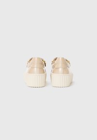 Chaussures à plateforme beige avec des sangles en cuir brillant, des accents en métal doré et des semelles texturées crème. Forme arrondie à l'arrière.