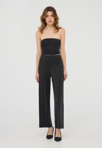 Top nero senza spalline con pois bianchi, abbinato a pantaloni palazzo neri a vita alta. La modella indossa dei tacchi neri con texture.