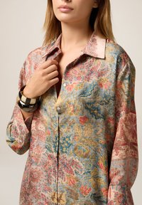 Losse, bloempatronen shirt in pastelkleuren (blauw, roze, geel) met een kraag en lange mouwen. Heeft een knoopsluiting en een gestructureerde stof.