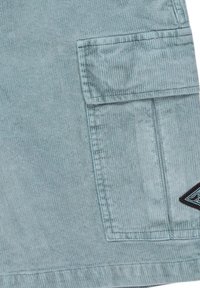 Lichtblauwe corduroy shorts met een grote zijzak en een zwart logo opdruk. De stof heeft een zachte, ribbelige textuur.