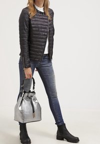 Chaqueta negra acolchada de corte slim, combinada con vaqueros azules. Sosteniendo un bolso tipo cubo metálico plateado, llevado con botines negros hasta el tobillo.