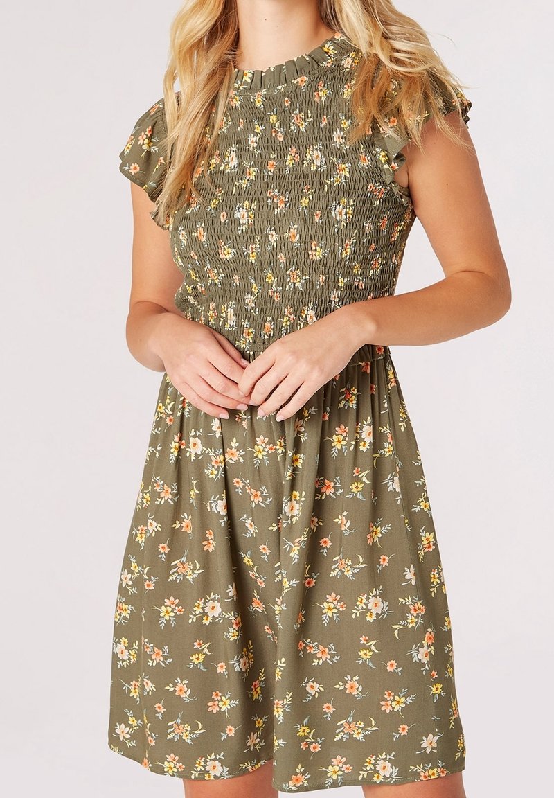Robe fleurie vert olive avec de courtes manches volantées, corsage smocké et jupe évasée ornée de petites fleurs blanches et oranges.
