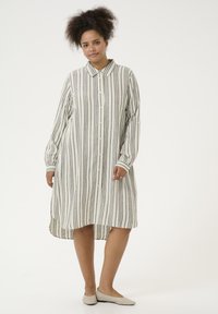 Abito a camicia a righe in crema e grigio, con chiusura a bottoni sul davanti, maniche lunghe con dettagli ai polsini e orlo asimmetrico.