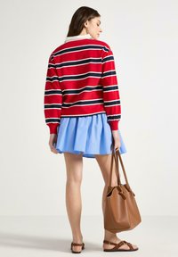 Maglione a righe rosse e blu navy con collo, abbinato a una gonna flare azzurra chiara e una borsa a tracolla marrone. Sandali beige completano il look.