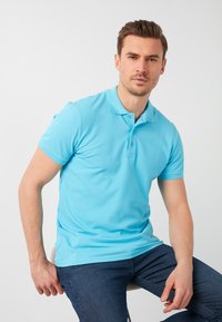 Svetlomodrá polo tričko vyrobené z hladkej bavlnenej látky, s krátkymi rukávmi, trojcvokovým zapínaním a priliehavým strihom na sediacom modeli.