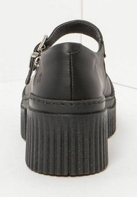 Zapato de plataforma de cuero negro con un respaldo redondeado, hebilla ajustable y suela acanalada. Textura suave con detalles de costura sutiles.