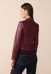 Bordeaux skinnjakke med en tettsittende design, som har jevn tekstur og stående krage, sammen med mørkeblå jeans.