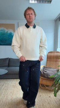 Sweatshirt crème avec col vert foncé, associé à un pantalon en denim bleu foncé. La tenue présente une coupe décontractée et une esthétique casual.