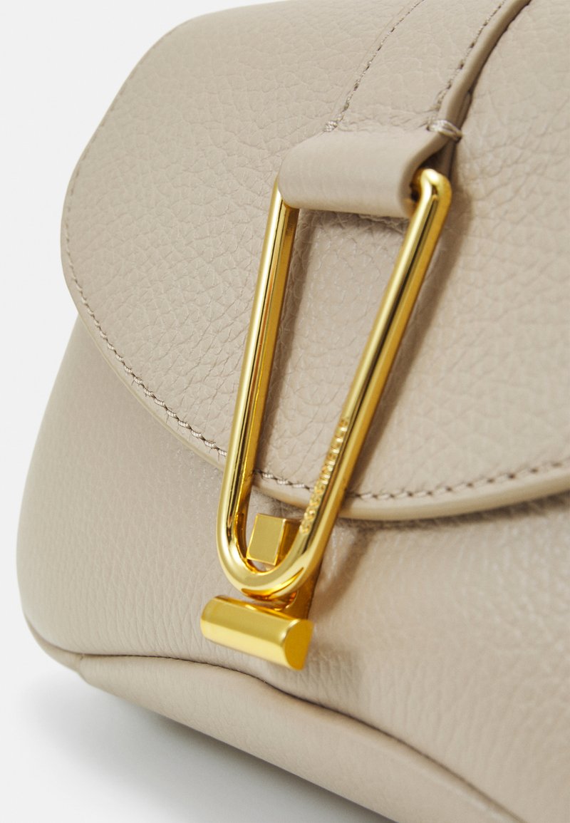 Beige Lederhandtasche mit strukturierter Oberfläche und einem auffälligen Beschlag aus goldfarbenem Metall. Abgerundete Kanten und minimalistische Steppnähte.