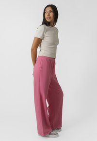 T-shirt ajusté gris clair à manches courtes, associé à un pantalon de survêtement rose à jambe large avec taille élastique et poches latérales.