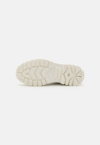Semelle de sneaker blanche avec une surface en caoutchouc texturée, comportant de profonds rainures, des motifs circulaires et des crampons distincts pour une meilleure adhérence.