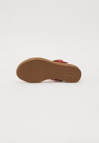 Rosa sandal med teksturert gummisåle, med bred stroppdesign og sirkulær accent. Materialet ser mykt ut med en glatt finish.