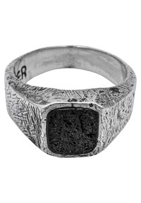 Sudraba gredzens ar teksturētu joslu, kurā ir kvadrāts melns akmens centrs. Akmens ir porains un ir iestiprināts nedaudz paceltā apvalkā.